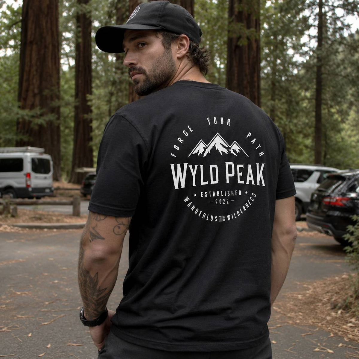 Man wearing a black t-shirt with 'Wyld Peak' logo in a forest setting