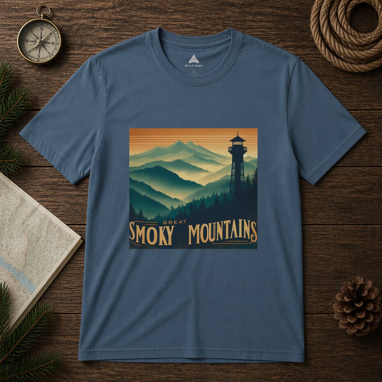Blue t-shirt with Great Smoky Mountains design on a wooden surface with nature-themed items.