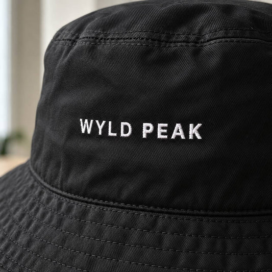 Close-up of a black bucket hat with 'WYLD PEAK' embroidered in white capital letters on the front panel.