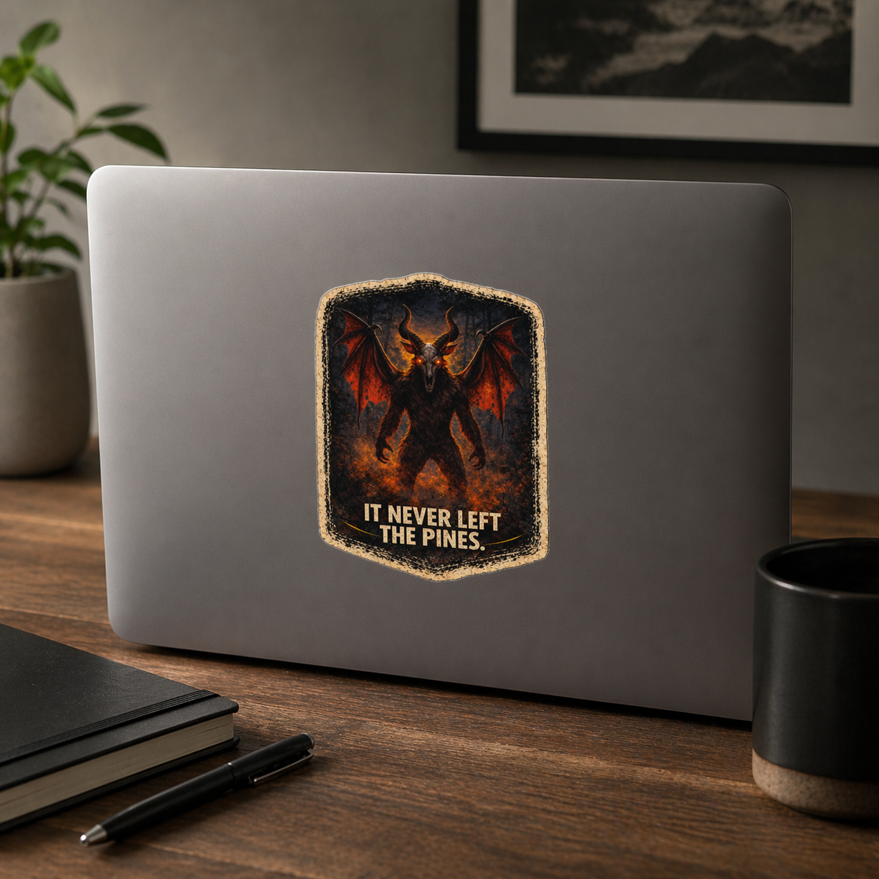 Laptop with a dragon sticker on a wooden desk with a plant and mug in the background