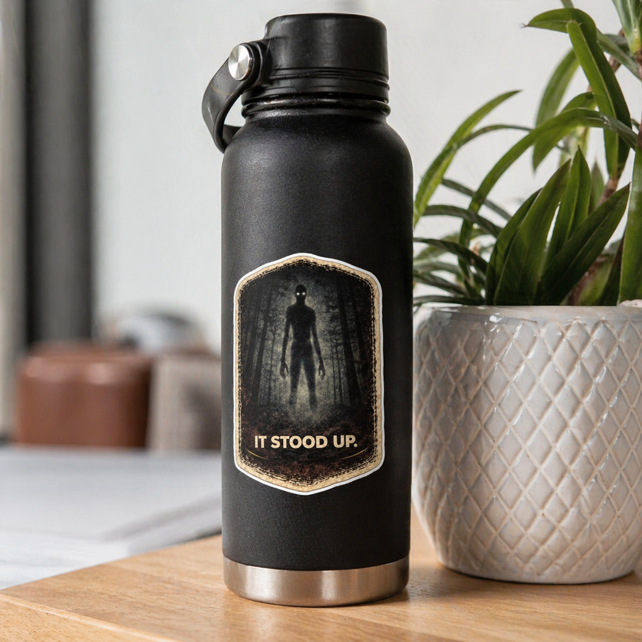 Black water bottle with a label on a wooden surface with a plant in the background