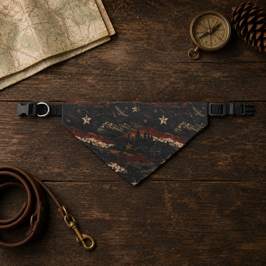 Dog bandana with mountain design on a wooden surface with map, compass, and pine cone.