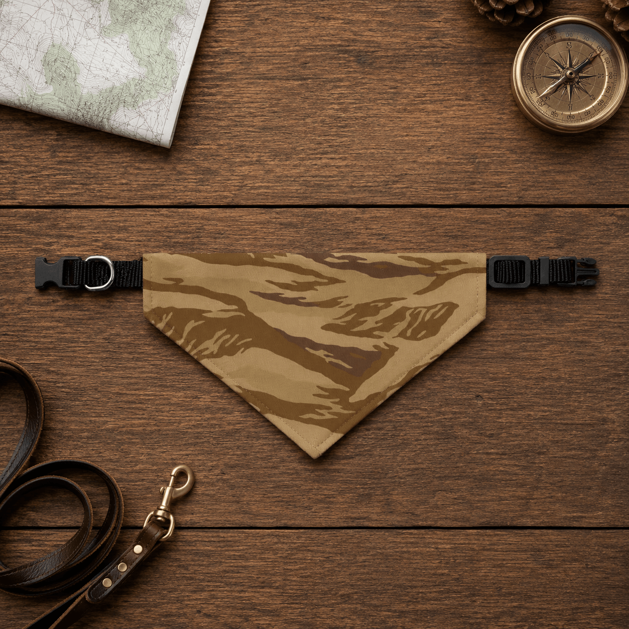 Camouflage dog bandana on a wooden surface with a map, compass, and leather leash.