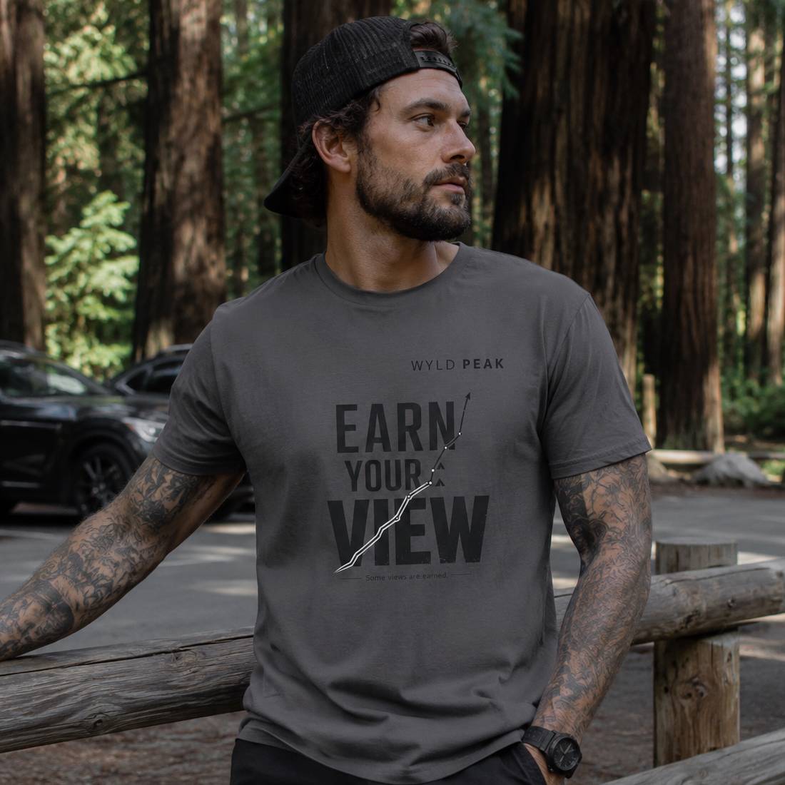 Man wearing a dark gray t-shirt with 'Earn Your View' text in a forest setting