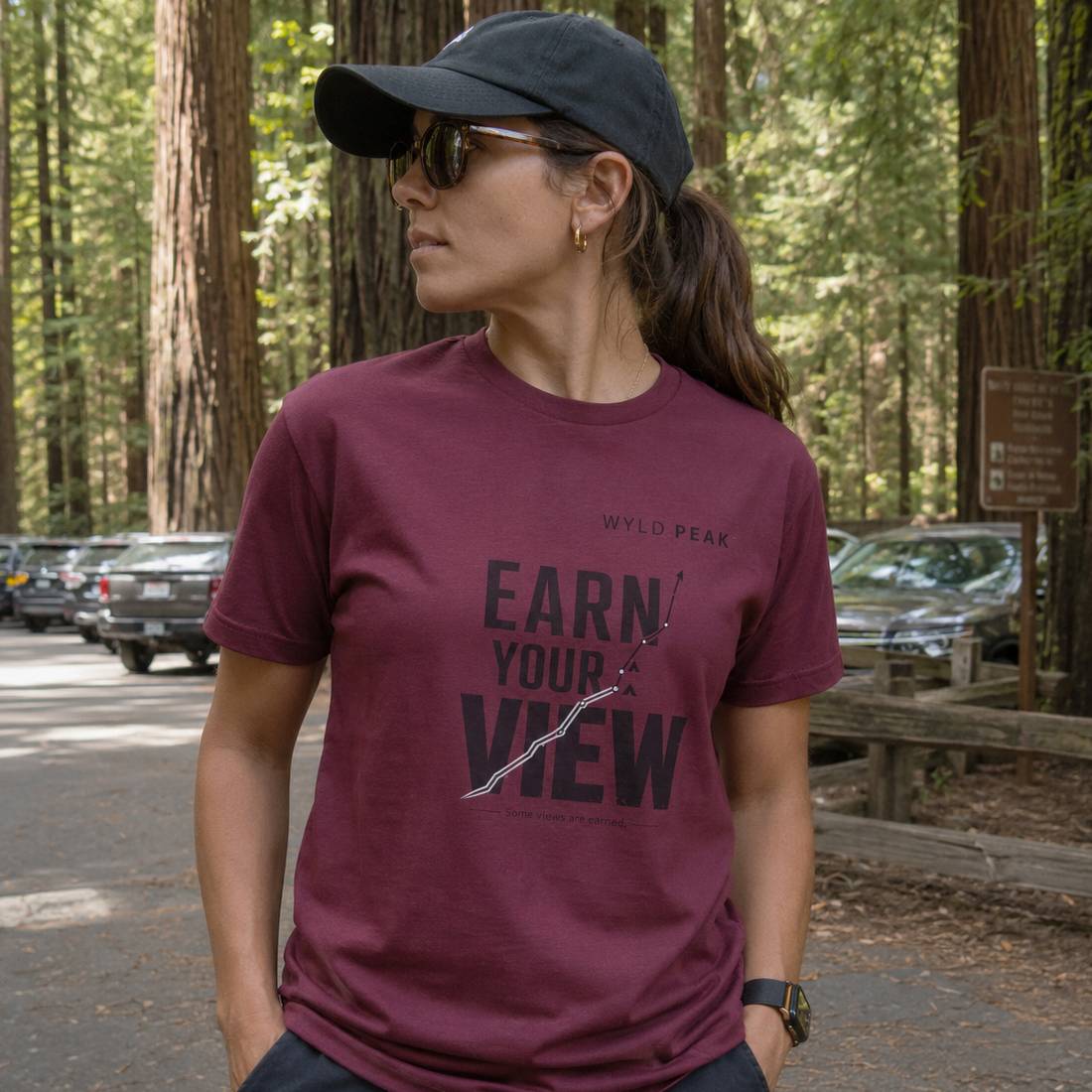 Woman wearing a maroon t-shirt with 'Earn Your View' text in a forest setting