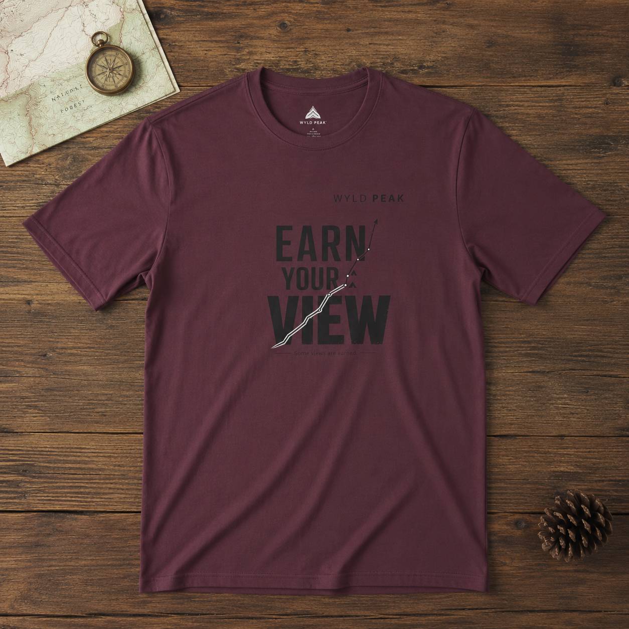Maroon t-shirt with 'Earn Your View' text on a wooden surface