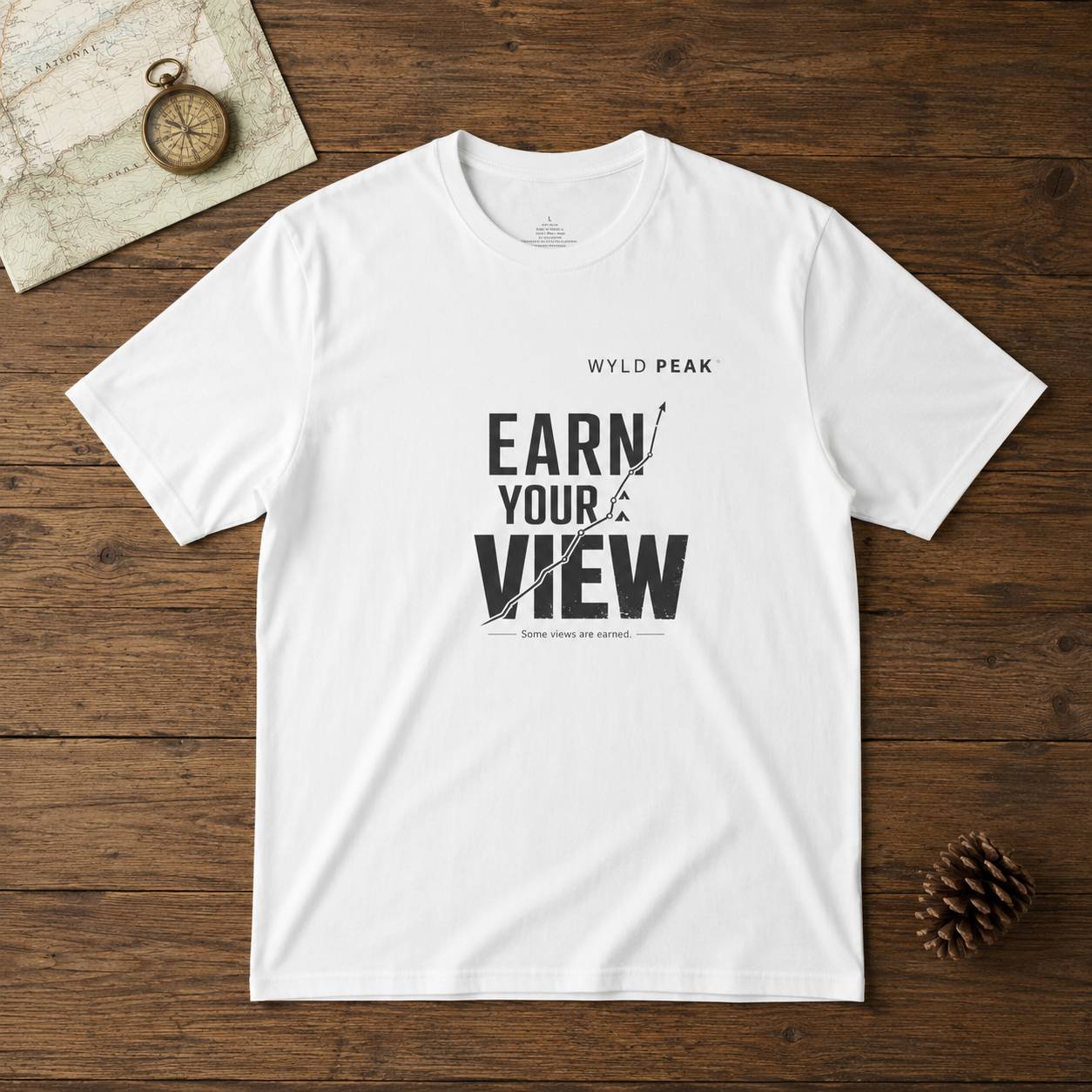 White t-shirt with 'Earn Your View' text on a wooden surface with a compass and map.