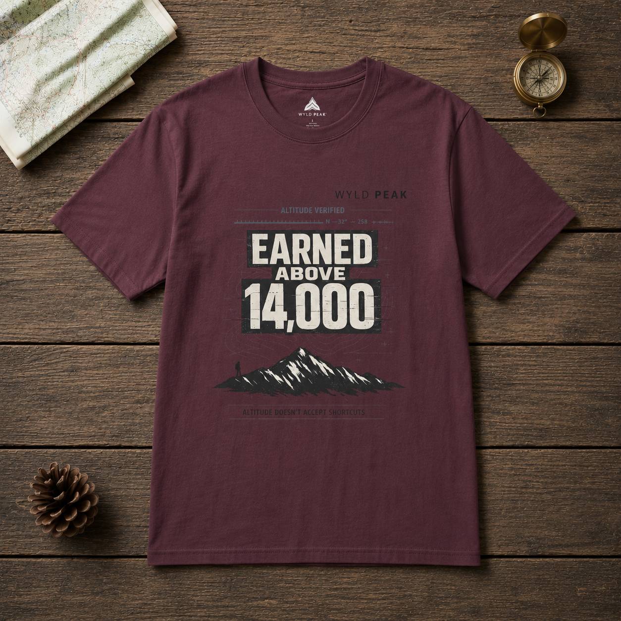 Maroon t-shirt with mountain graphic and text on a wooden surface