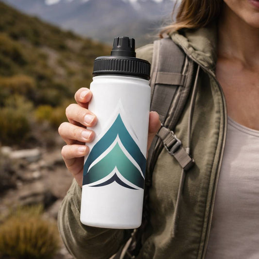 Person holding a white water bottle with a green and blue design in a mountainous outdoor setting