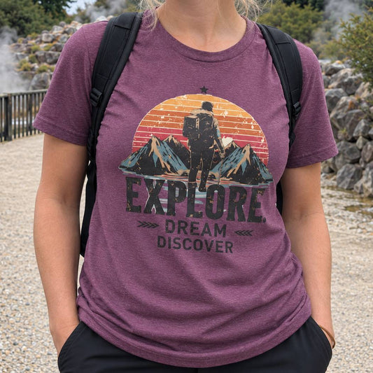 A person wearing a heathered purple graphic t-shirt with a hiking sunset design and the words 'EXPLORE. DREAM DISCOVER'.