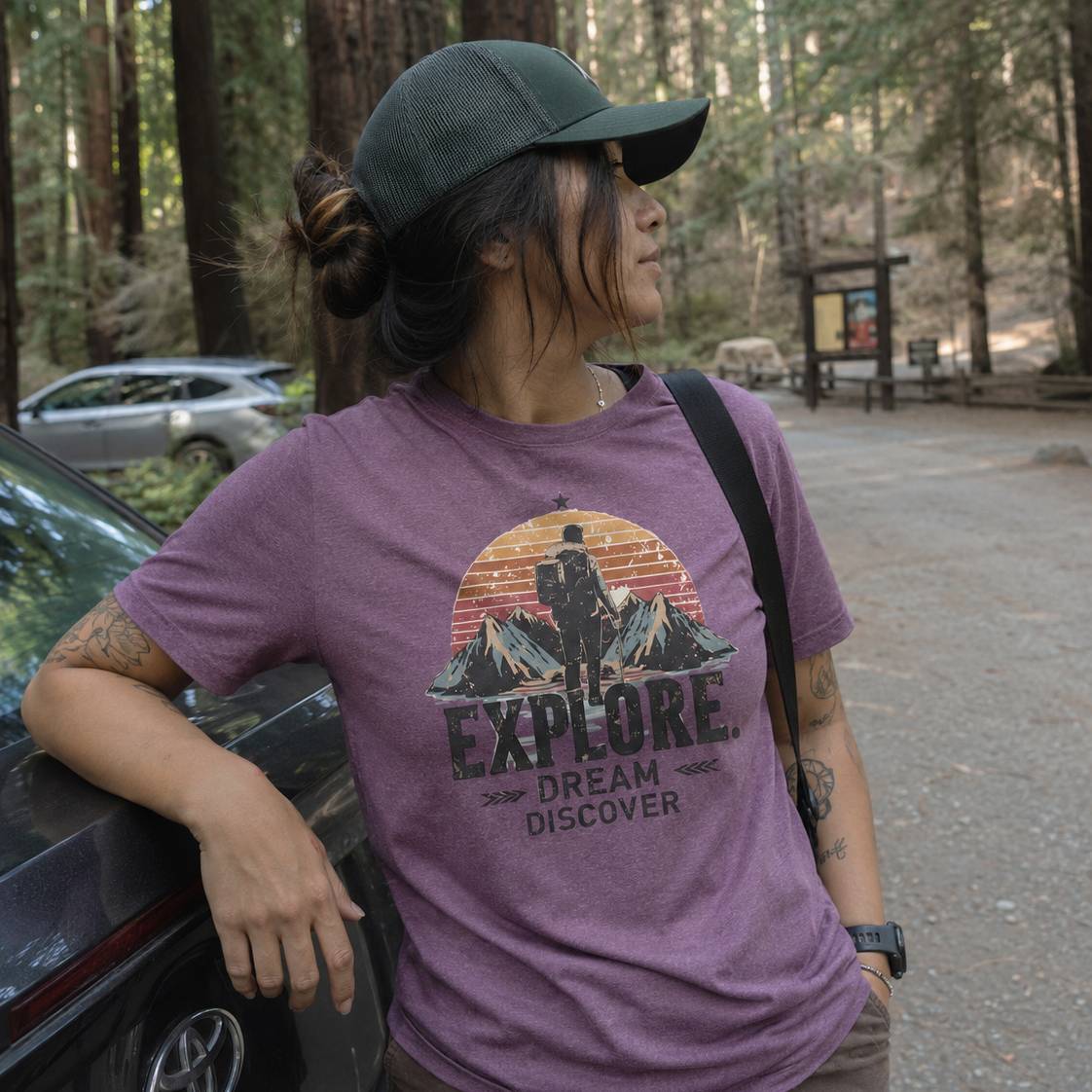 Person wearing a purple t-shirt with an 'Explore Dream Discover' design in a forest setting.