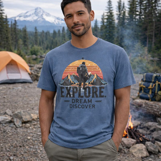 Man wearing a blue t-shirt with outdoor design and text, standing in a camping setting with mountains and trees.