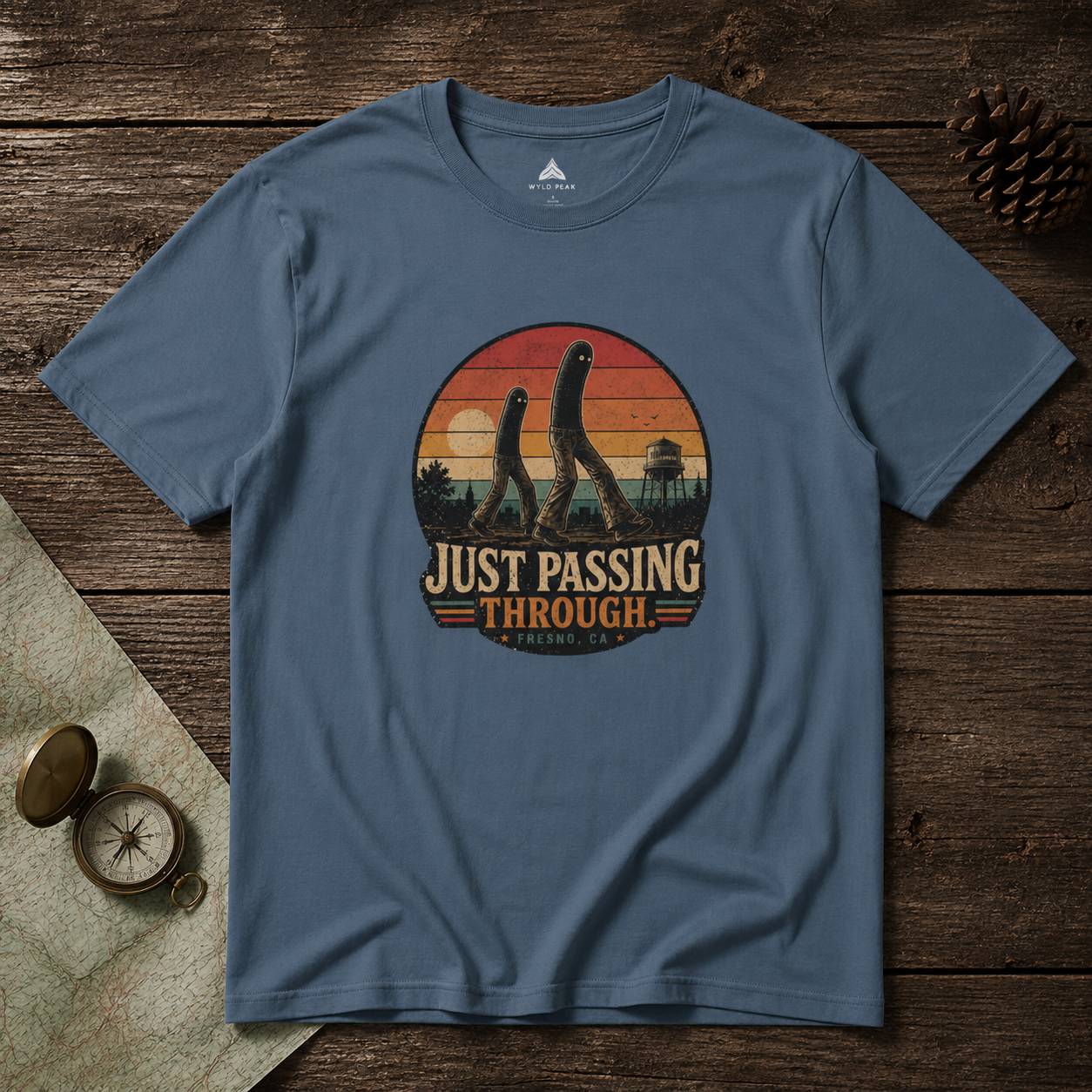 Blue t-shirt with 'Just Passing Through' fresno nightcrawler graphic on a wooden surface