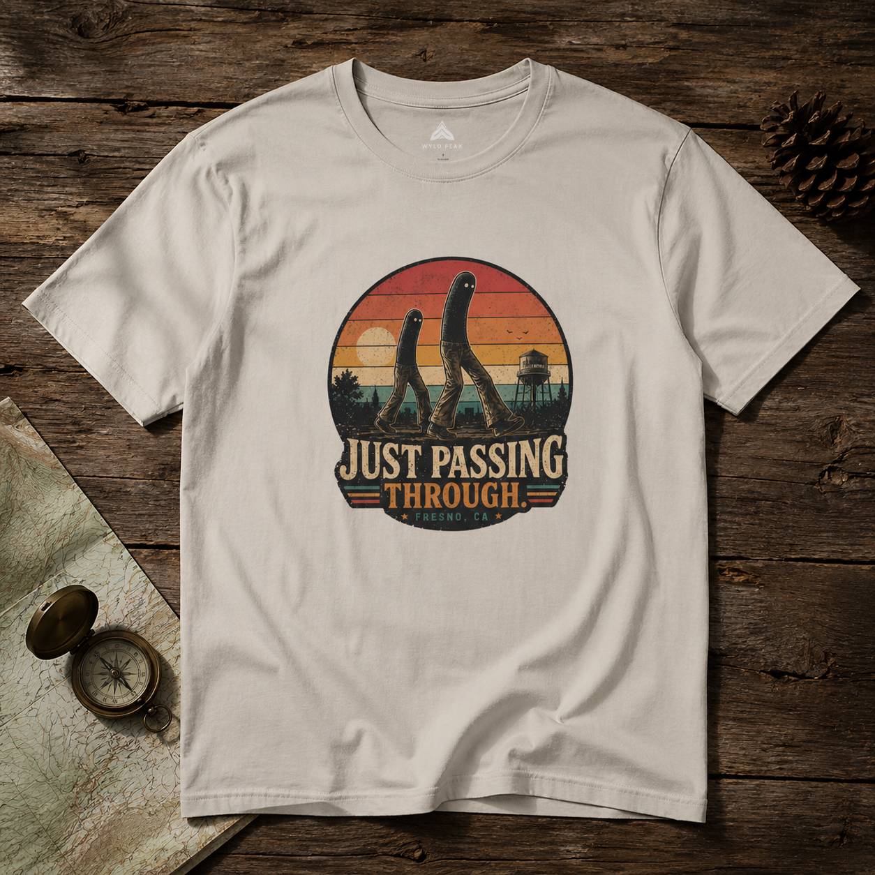 Beige t-shirt with 'Just Passing Through' fresno nightcrawler graphic on a wooden surface