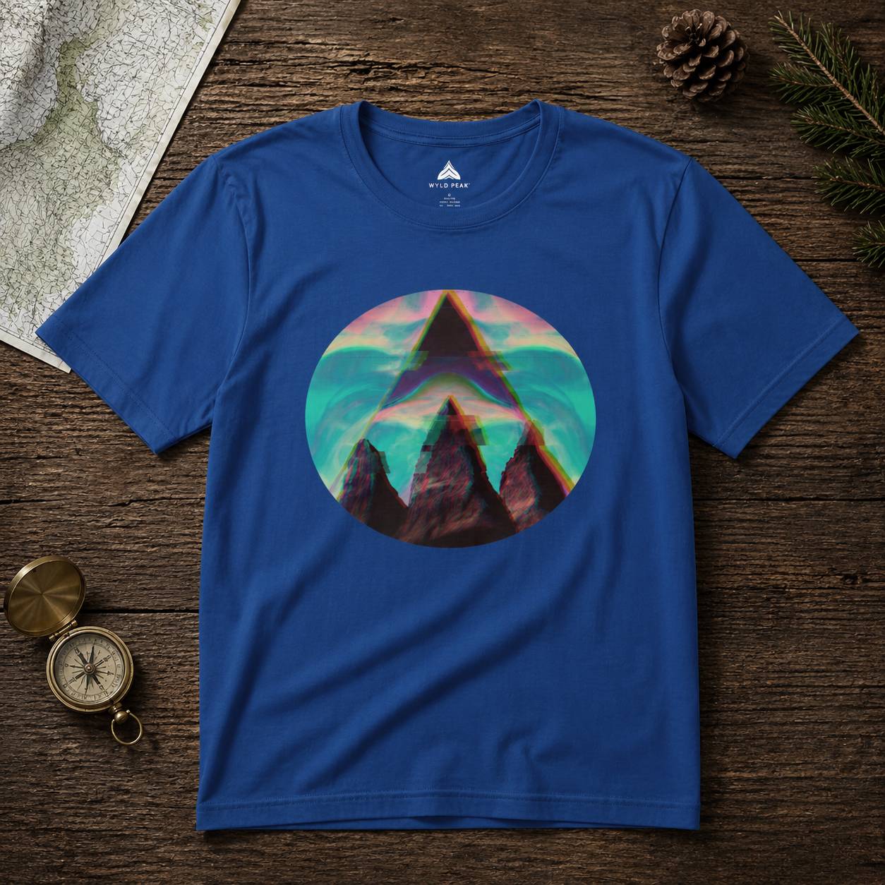 Blue t-shirt with a colorful mountain graphic on a wooden surface with nature-themed items.