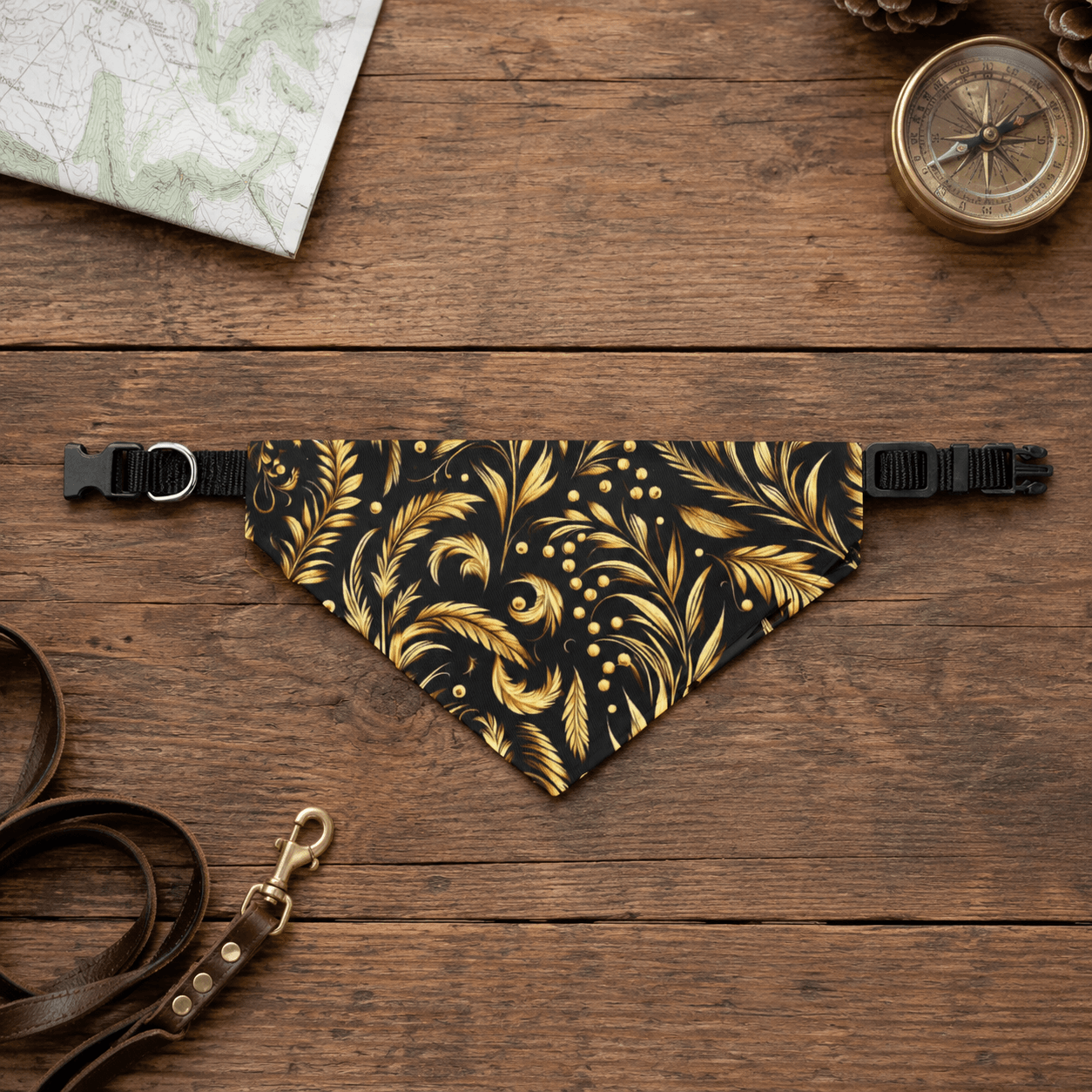 Black and gold patterned dog bandana on a wooden surface with a leash and compass.