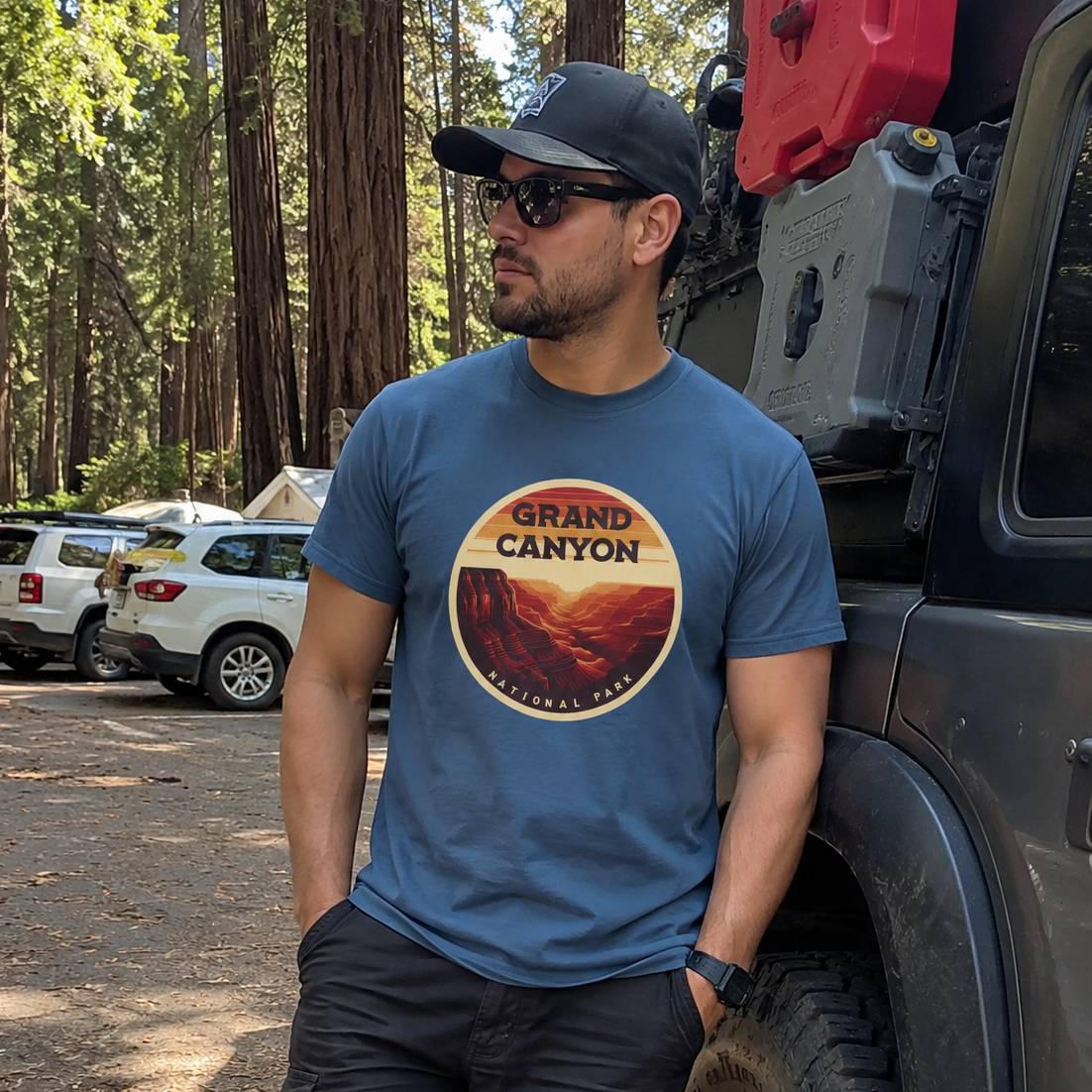 Man wearing a blue 'Grand Canyon' t-shirt standing next to a vehicle in a forest setting.