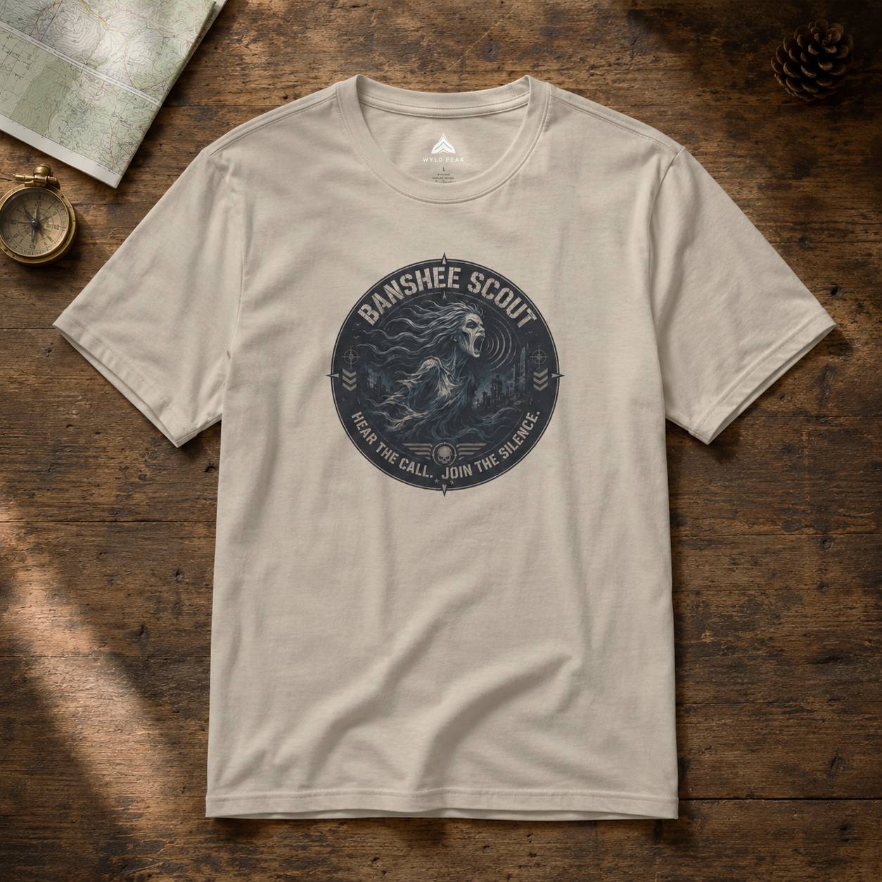 Beige t-shirt with 'Banshee Scout' graphic on a wooden surface