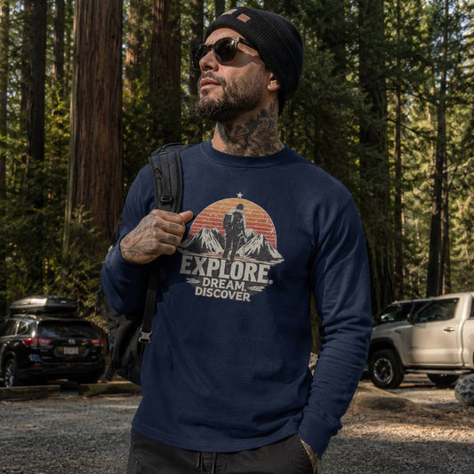 Man wearing a navy sweatshirt with 'Explore. Dream. Discover' graphic in a forest setting.