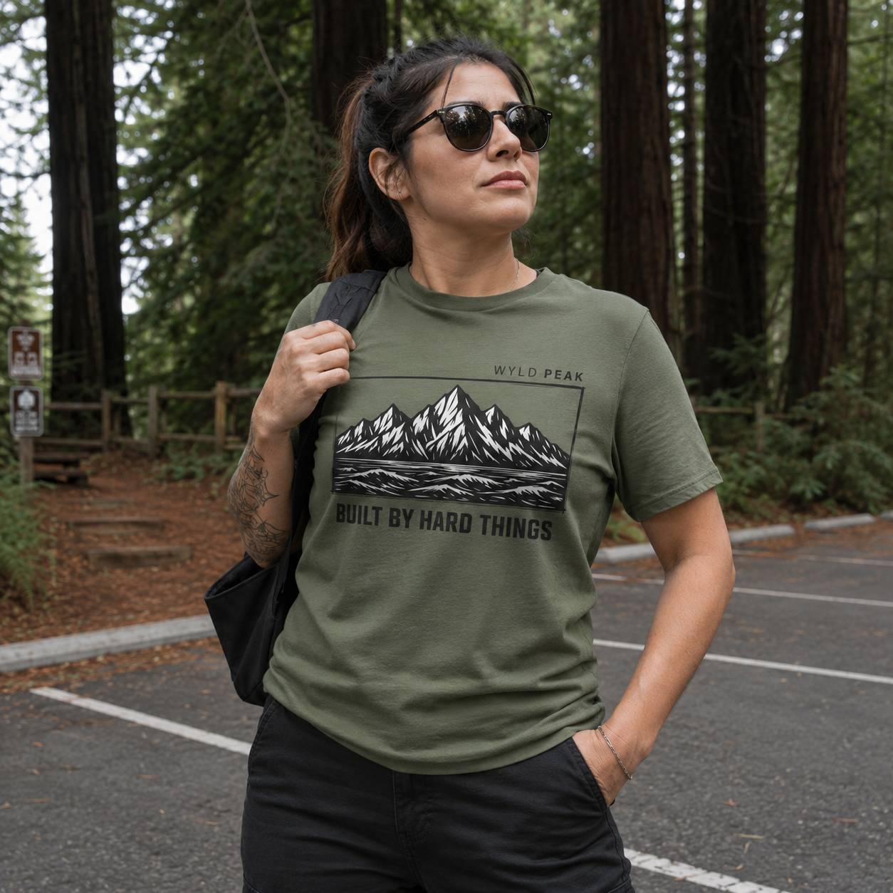 Woman wearing a green t-shirt with a mountain design in a forest setting