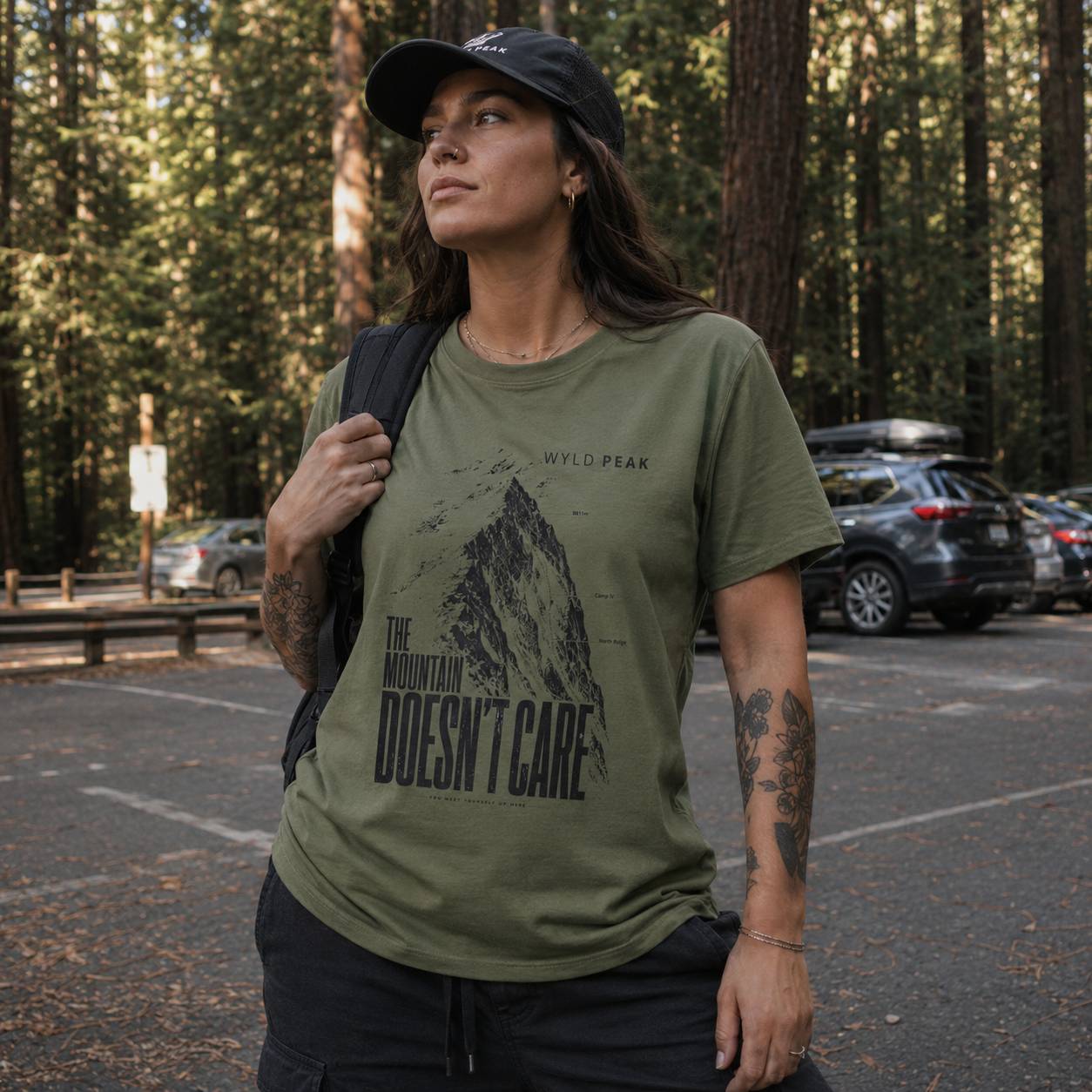 Person wearing a green t-shirt with a mountain graphic and text in a forest setting.