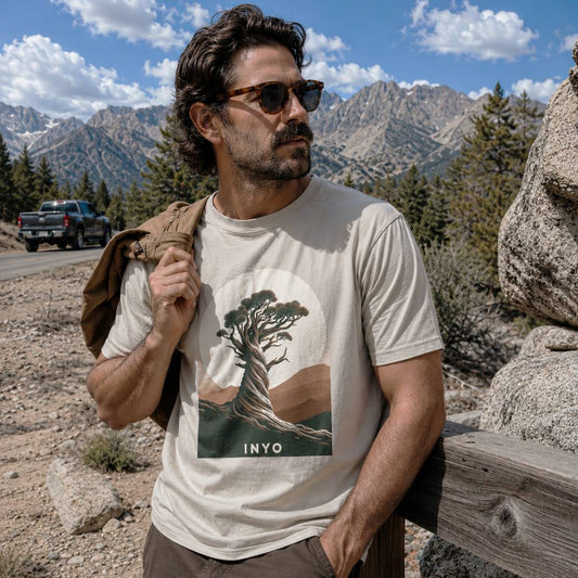 Man wearing a t-shirt with a tree design and 'Inyo' text, standing in a mountainous landscape.