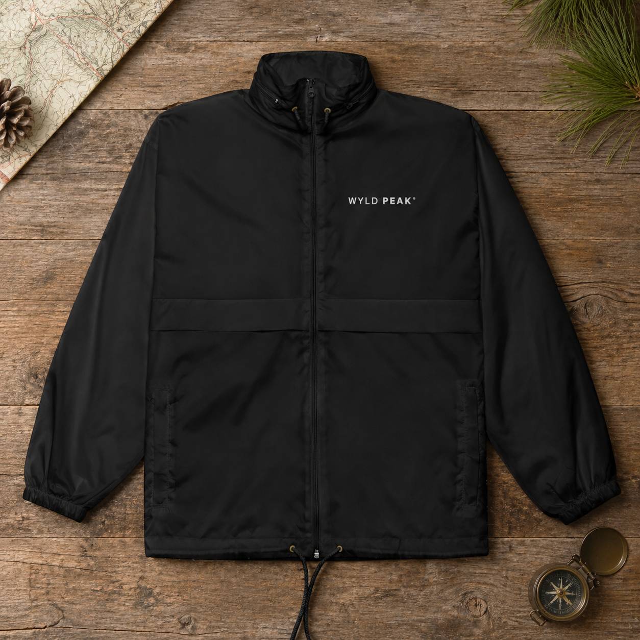 Black jacket with 'WYLD PEAK' logo on a wooden surface with nature-themed items.