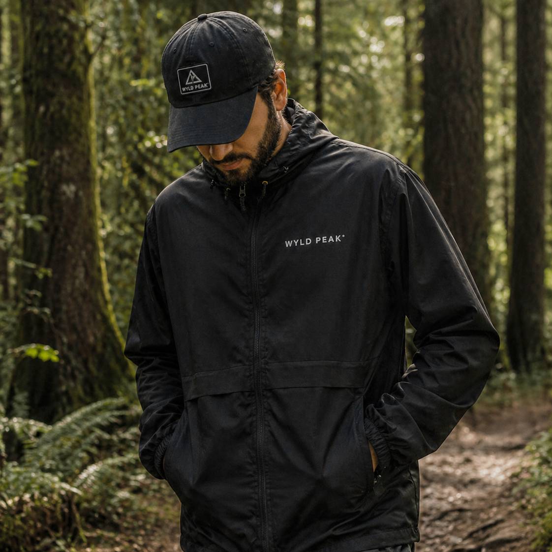 Man wearing a black jacket and cap with 'Wyld Peak' branding in a forest setting