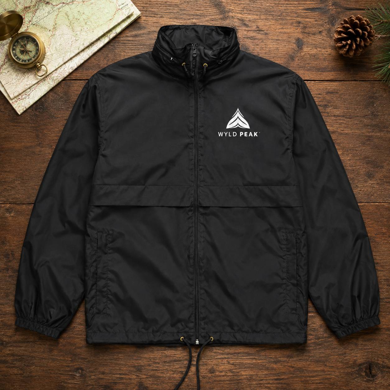 A black lightweight zip-front jacket laid flat on a rustic wooden surface, with a white Wild Peak mountain logo printed on the left chest. The jacket has a stand collar, front zipper, elasticized cuffs and hem, and side pockets.