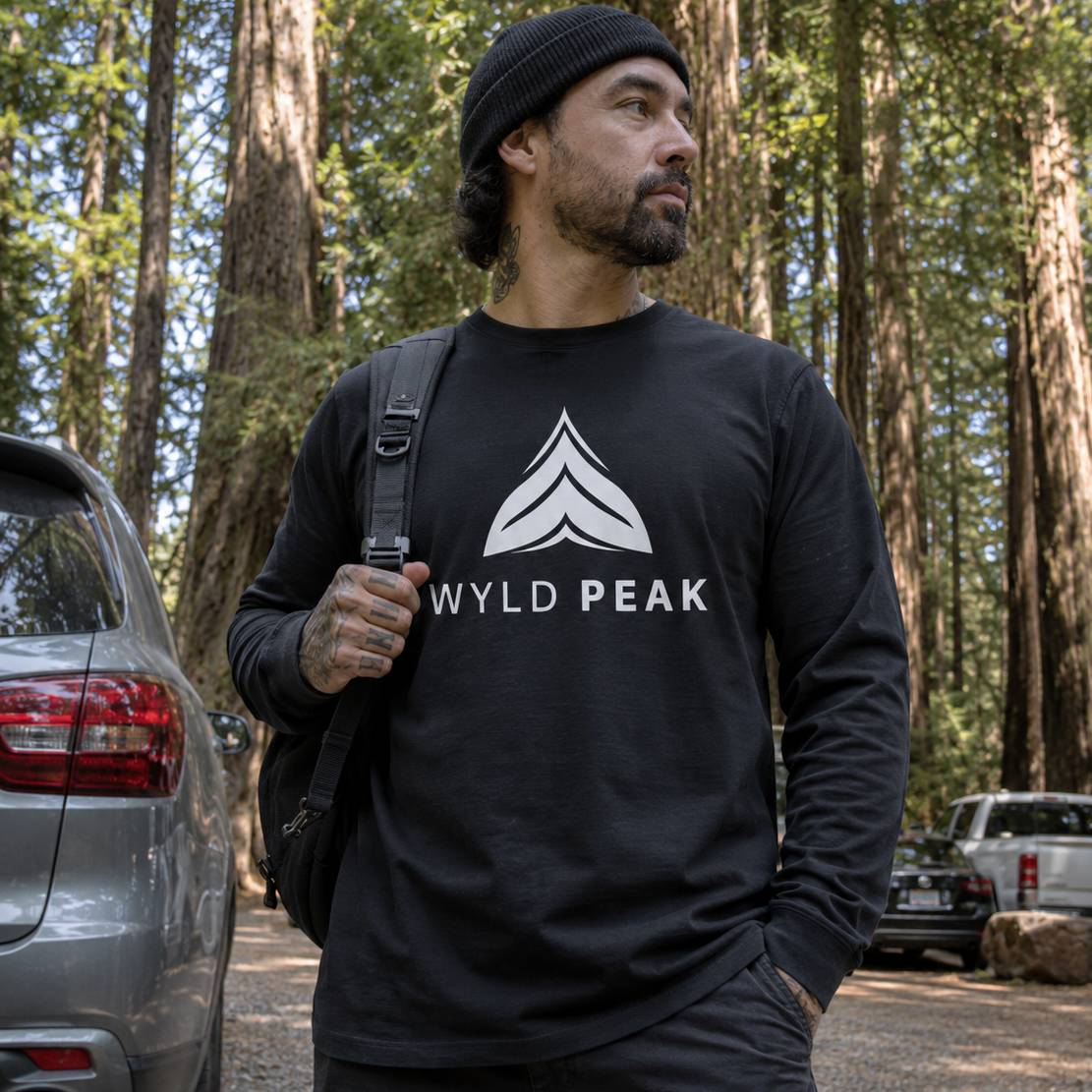 Man wearing a black 'Wyld Peak' sweatshirt in a forest setting.
