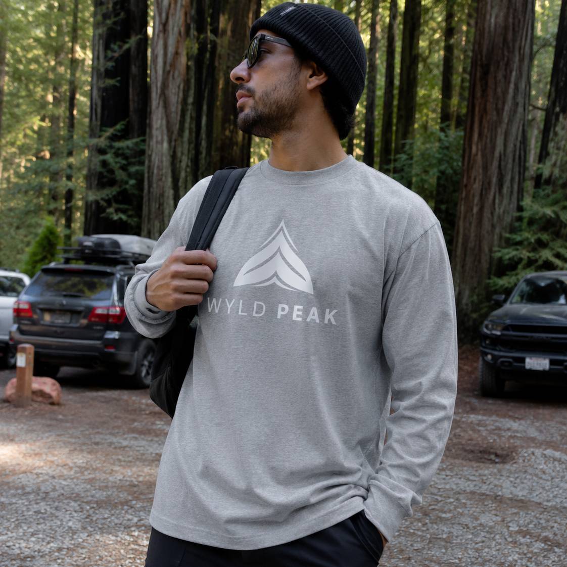 Man wearing a gray 'WYLD PEAK' shirt in a forest setting