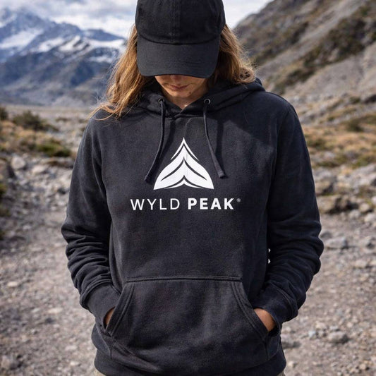 Person wearing a black hoodie with 'Wyld Peak' logo in a mountainous landscape