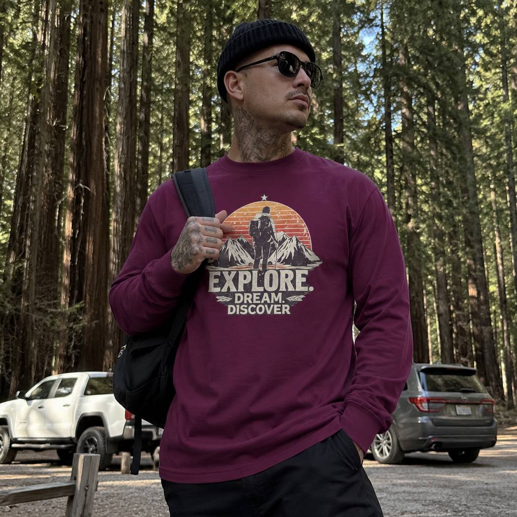 Man wearing a maroon sweatshirt with an 'Explore' graphic in a forest setting
