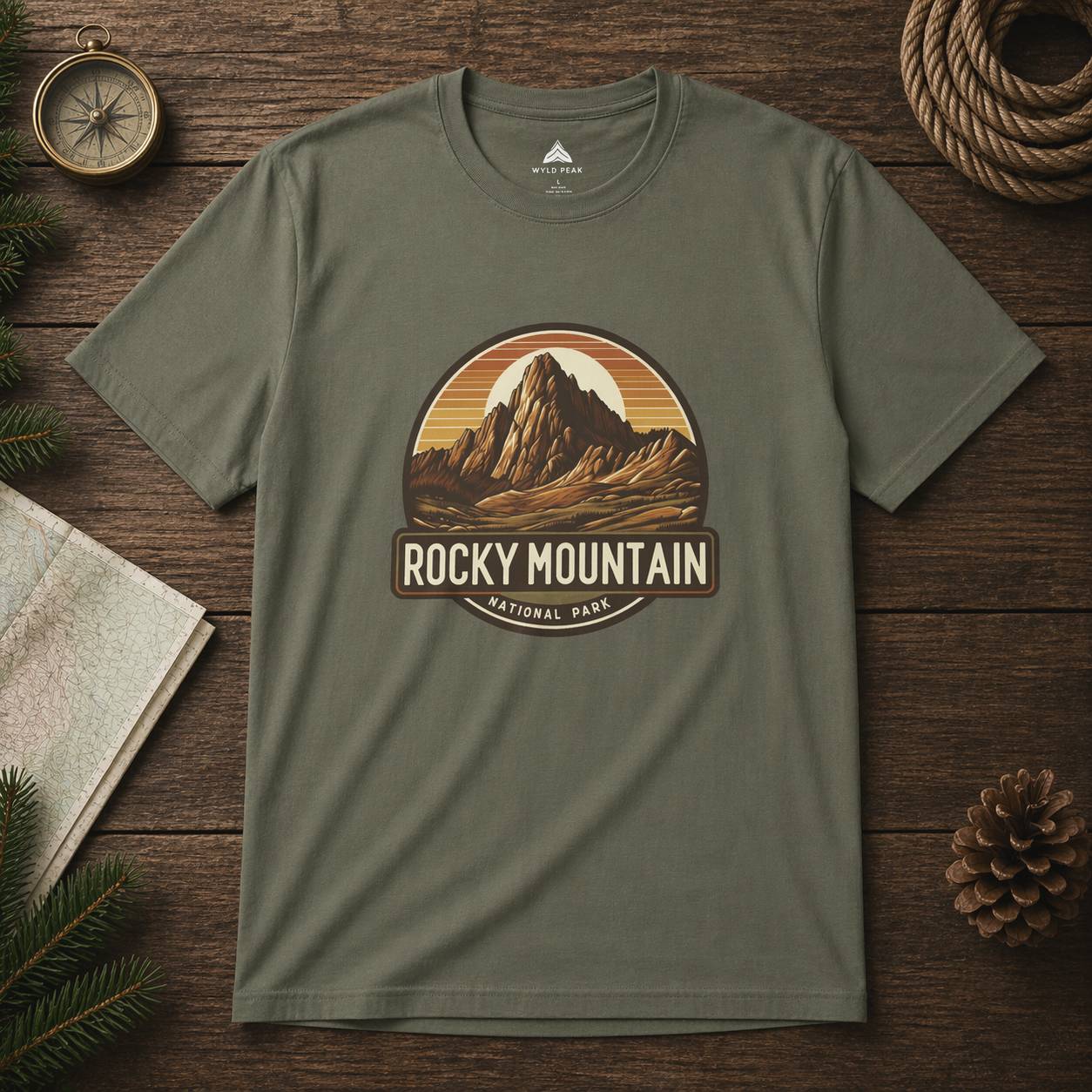 Green t-shirt with Rocky Mountain National Park graphic on a wooden surface with nature-themed items.