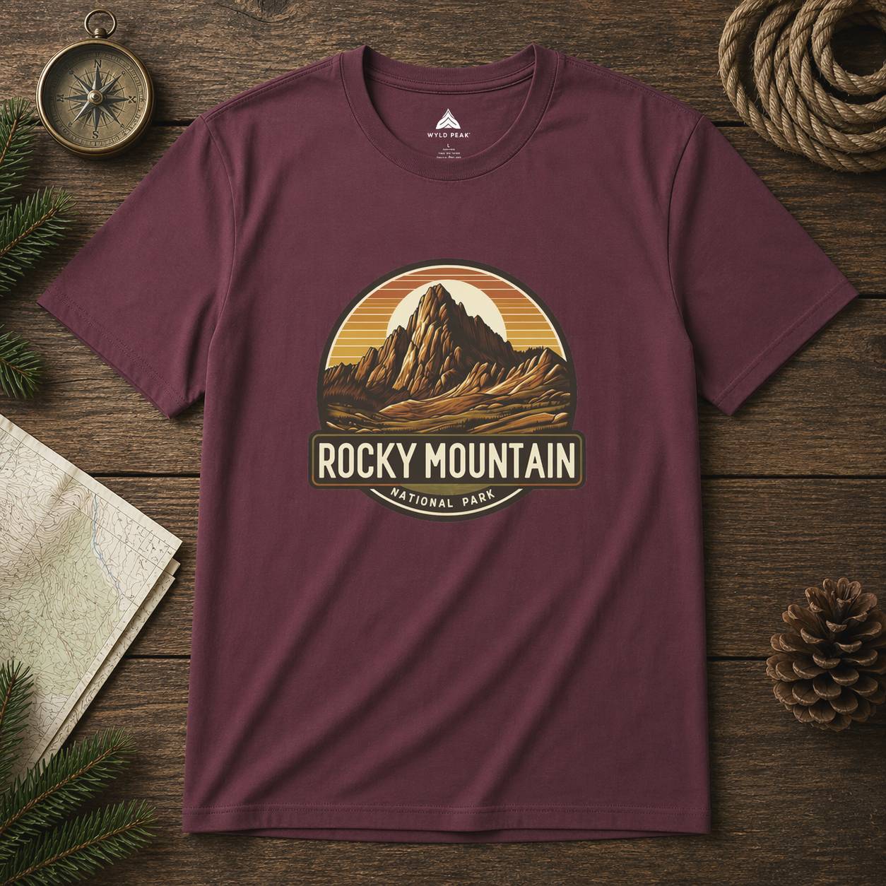 Maroon t-shirt with Rocky Mountain National Park graphic on a wooden surface with nature-themed items.