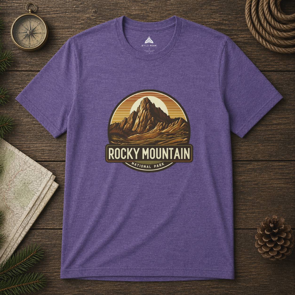Purple t-shirt with Rocky Mountain National Park graphic on a wooden surface with nature-themed items.