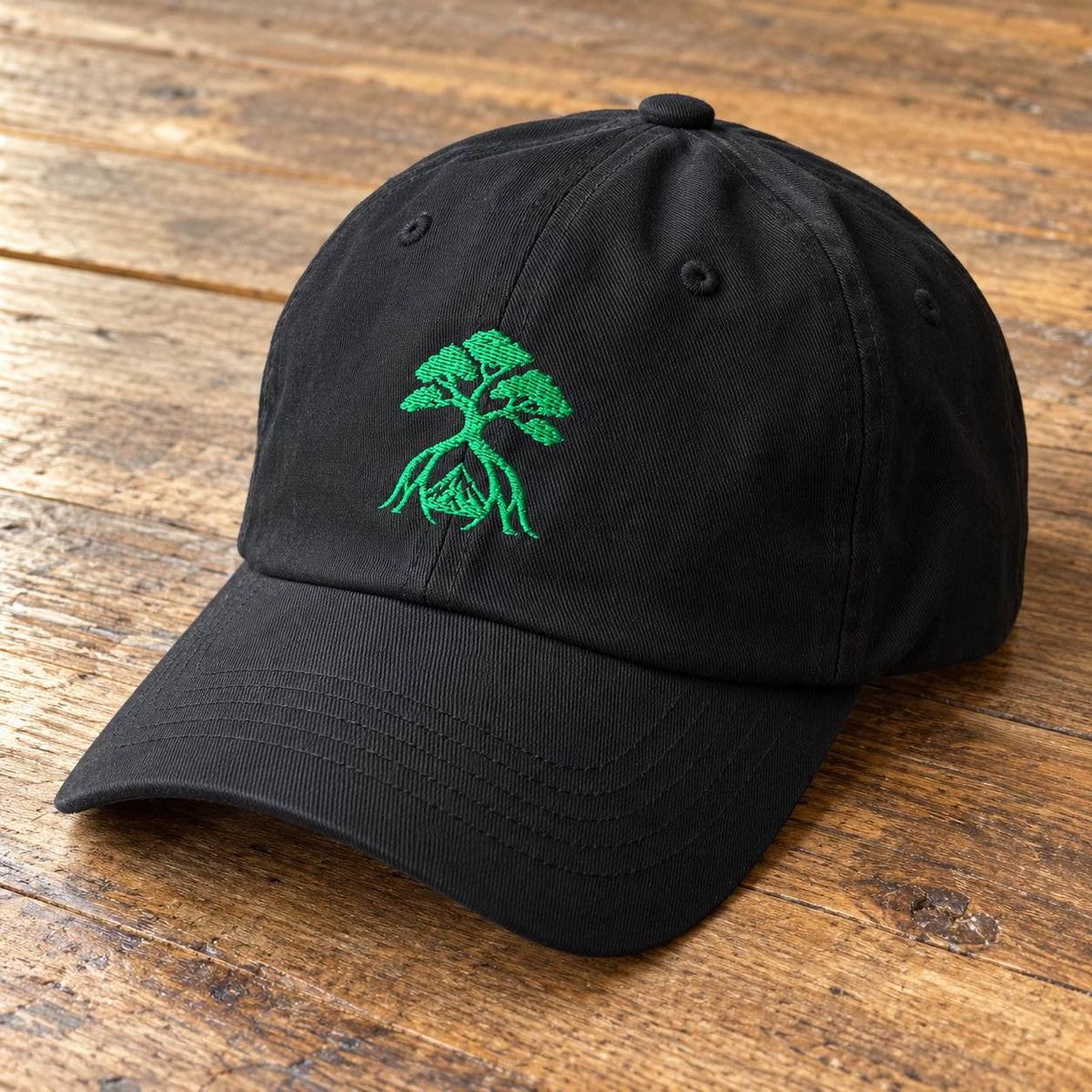 A black baseball cap with a green embroidered bonsai tree design on the front, resting on a rustic wooden surface.