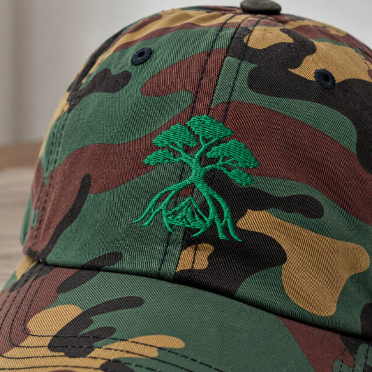 Close-up of a camouflage baseball cap with a green embroidered tree of life motif on the front panel.