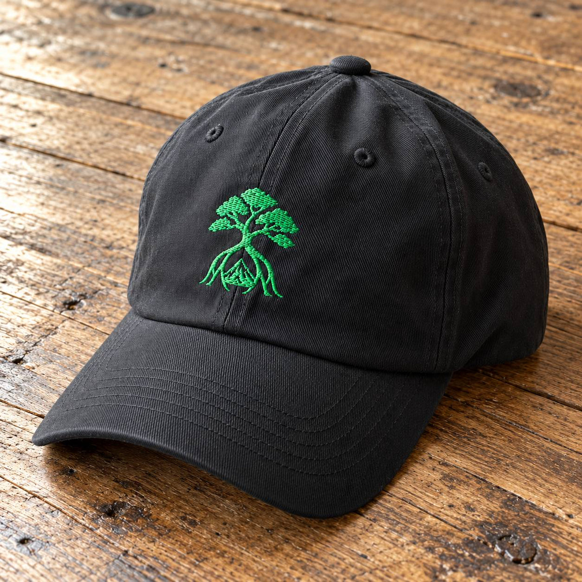 A black cotton baseball cap with a green embroidered bonsai tree design on the front, resting on a rustic wooden surface.