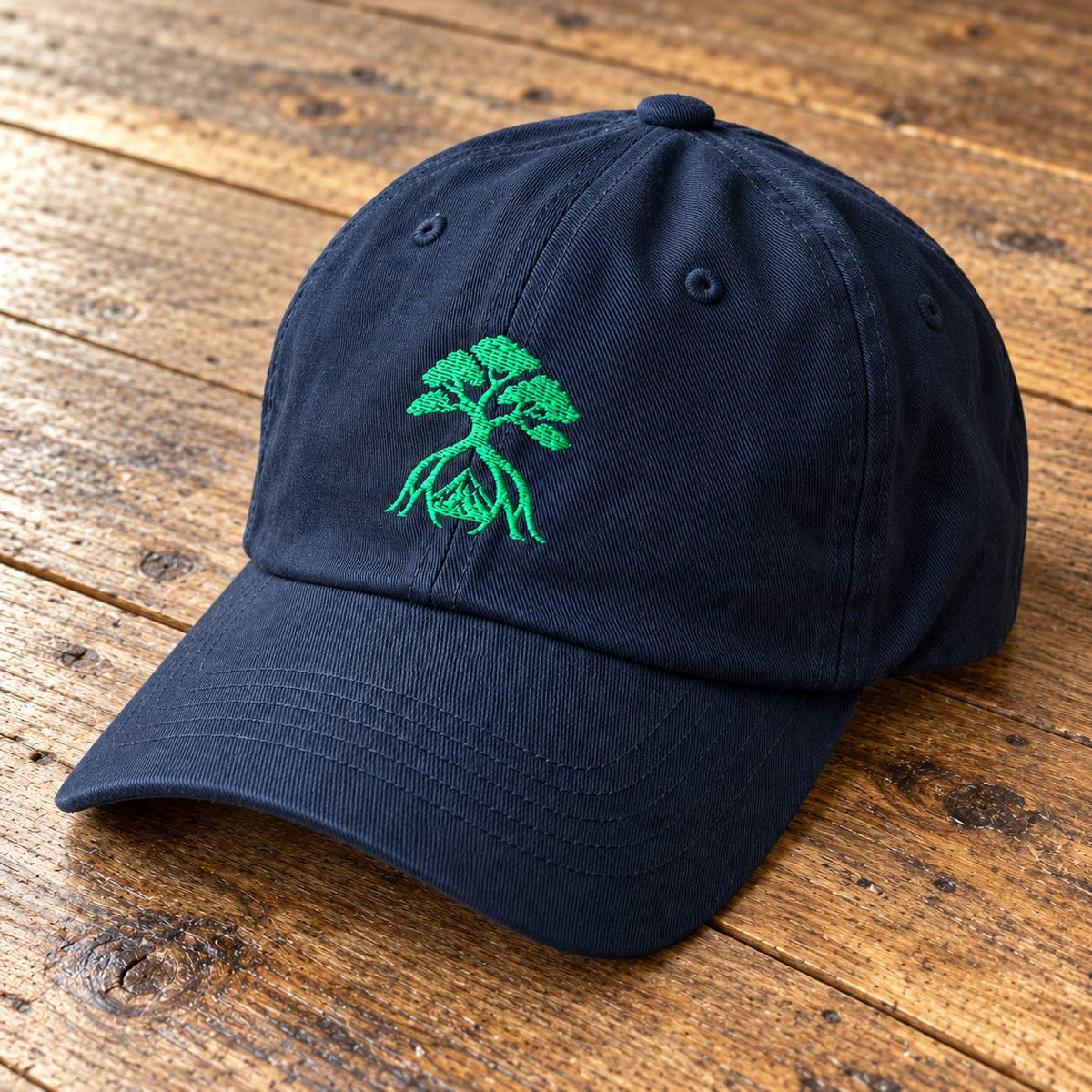 A dark navy blue baseball cap with a green embroidered bonsai tree design on the front, resting on a rustic wooden surface.