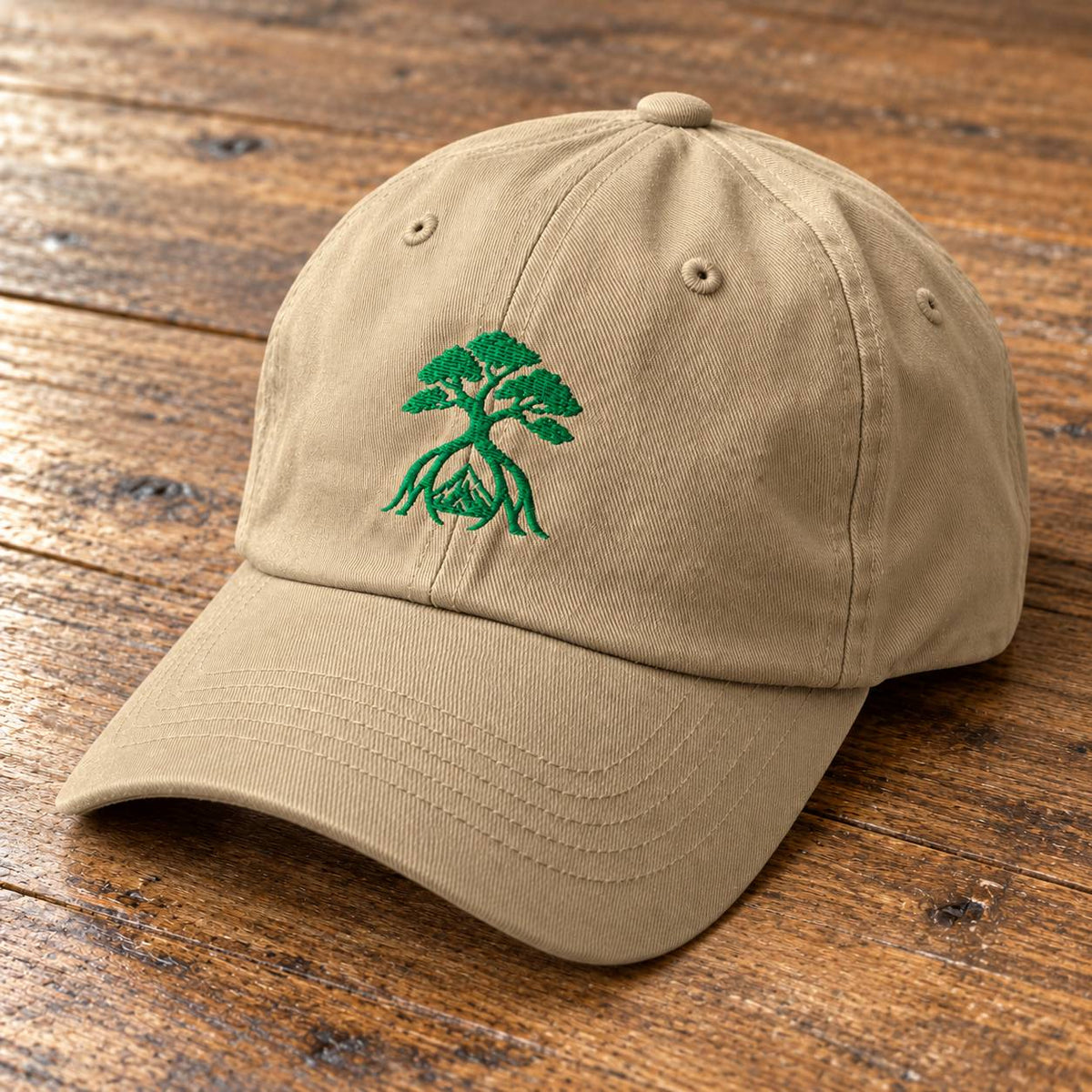 A beige baseball cap with a green embroidered bonsai tree design on the front, resting on a rustic wooden surface.