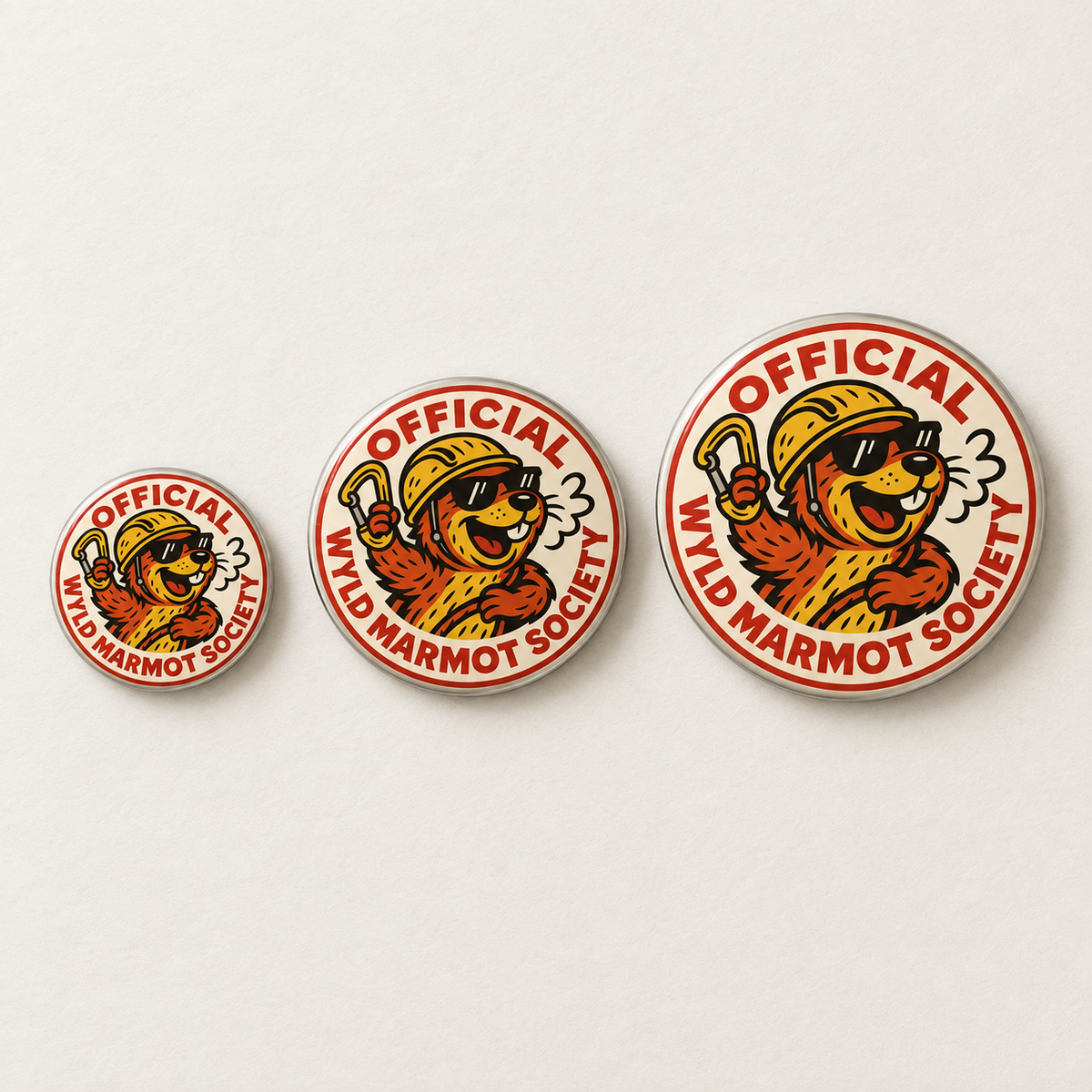 Three circular enamel pins of the 'Official Wyld Marmot Society' in graduated sizes, displayed on a clean off-white background.