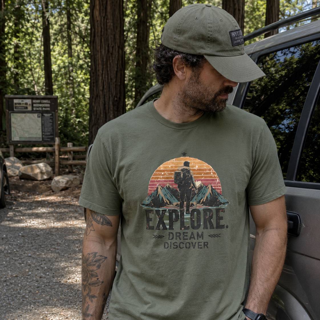 Man wearing a green t-shirt with 'Explore Dream Discover' graphic in a forest setting.