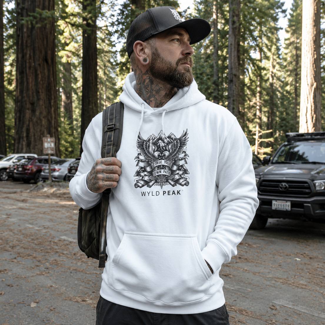 Man wearing a white hoodie with 'Wyld Peak' logo in a forest setting