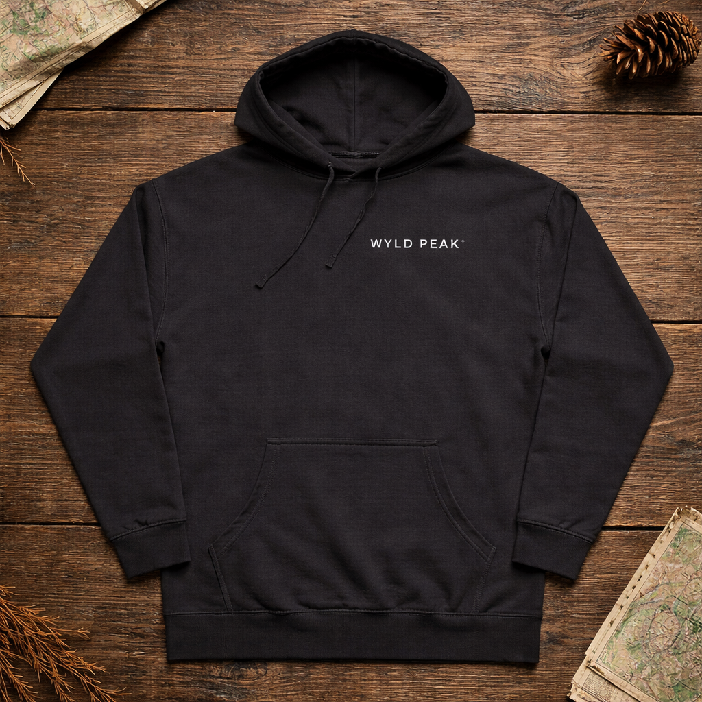 Black hoodie with 'Wyld Peak' logo on a wooden surface with nature-themed decorations.