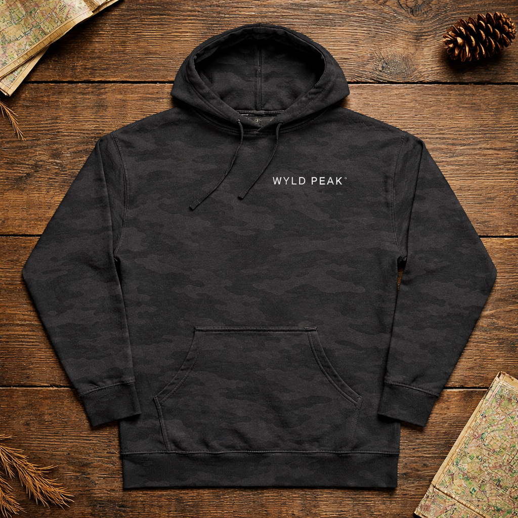 Black hoodie with 'WYLD PEAK' logo on a wooden surface with nature-themed decorations.