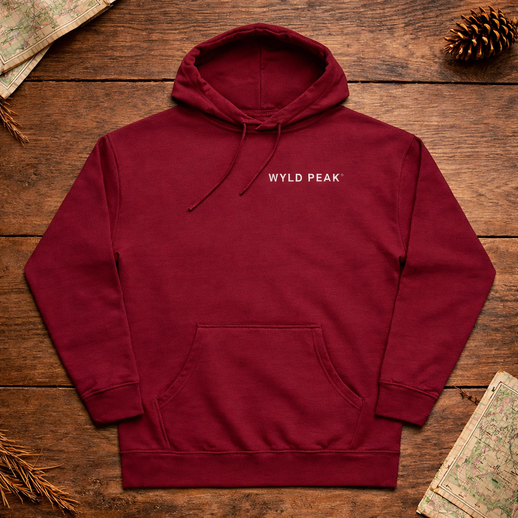 Maroon hoodie with 'Wyld Peak' logo on a wooden surface with nature-themed decorations.