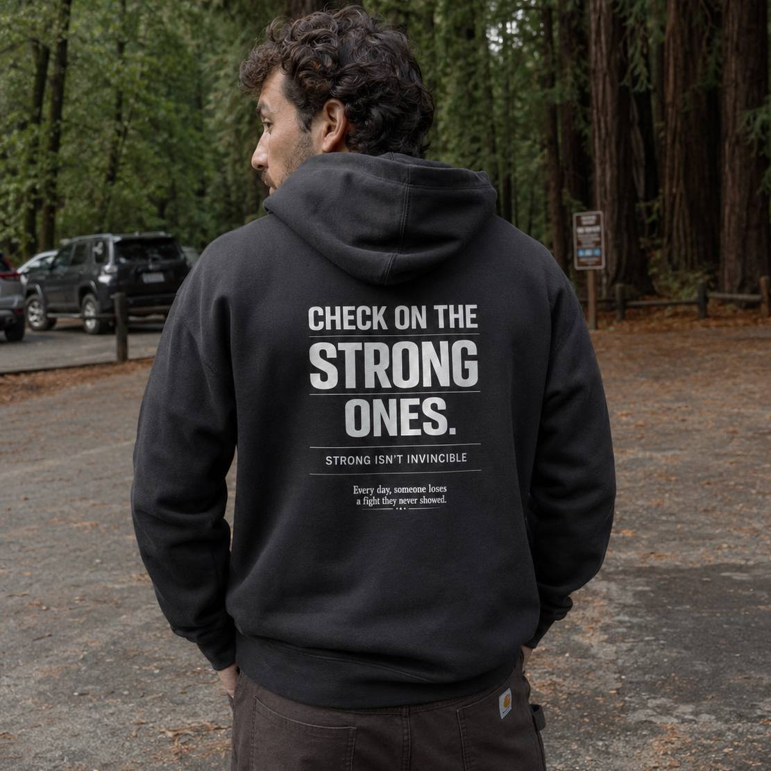 Man wearing a black hoodie with motivational text in a forest setting