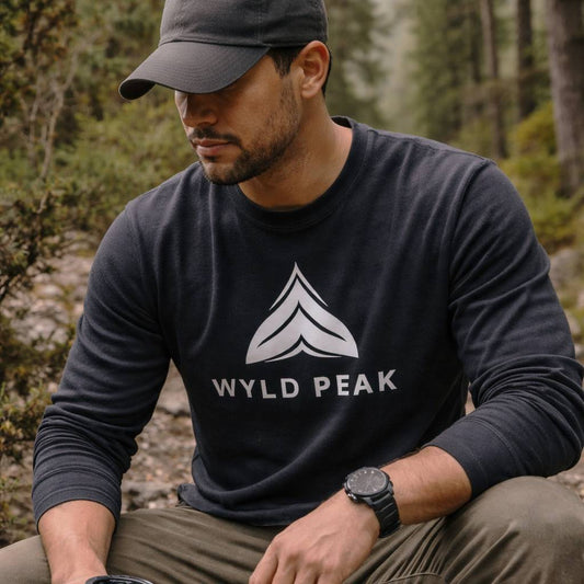 Man wearing a black 'Wyld Peak' sweatshirt sitting outdoors in a forest.