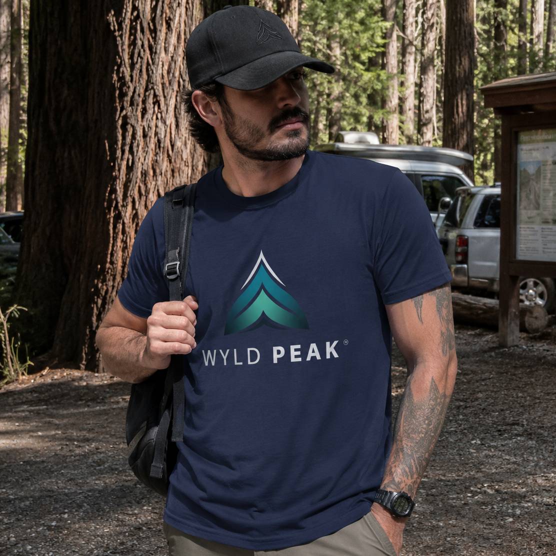Man wearing a navy blue 'Wyld Peak' t-shirt in a forest setting